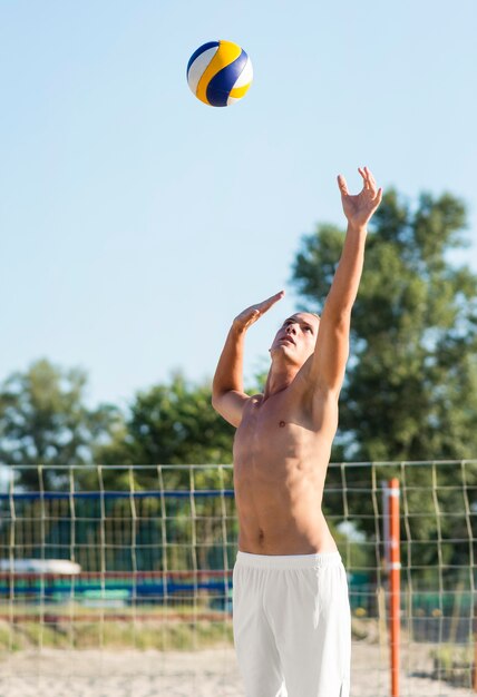 Shirtless mannelijke volleyballer op het strand spelen met de bal