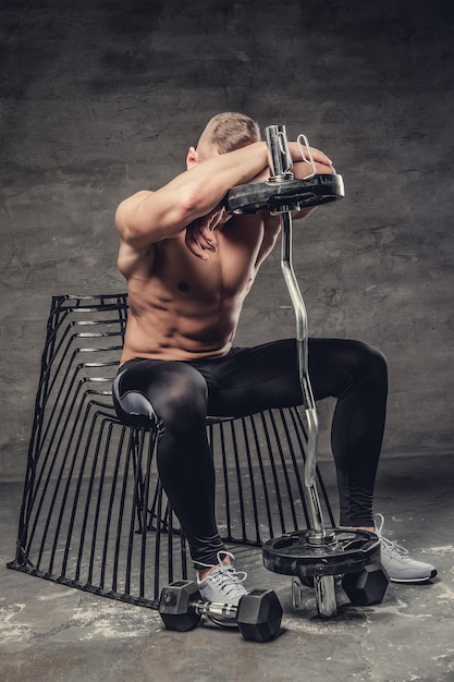 Shirtless sportieve man zittend op een stoel en halter te houden.