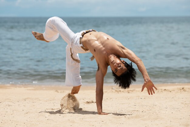 Shirtloze man die alleen capoeira beoefent op het strand