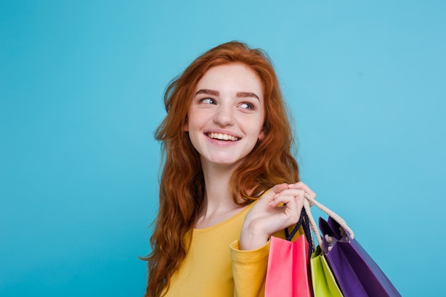 Shopping Concept - Close-up Portret jonge mooie aantrekkelijke roodharige meisje lachende camera kijken met boodschappentas. Blauwe Pastelachtergrond. Kopieer de ruimte.