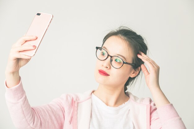 Shot in de studio van de jonge Aziatische vrouw om mobiele telefoon zelf timer te spelen