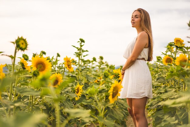 Shot van een aantrekkelijke blonde vrouw in een witte jurk poserend in een zonnebloemveld