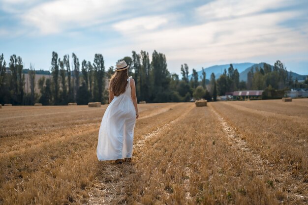 Shot van een aantrekkelijke jonge boerin in een witte jurk in een droog veld van stro