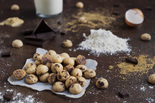 Shot van minikoekjes op perkamentpapier met chocoladerepen, bloem, eieren en melk op een tafel