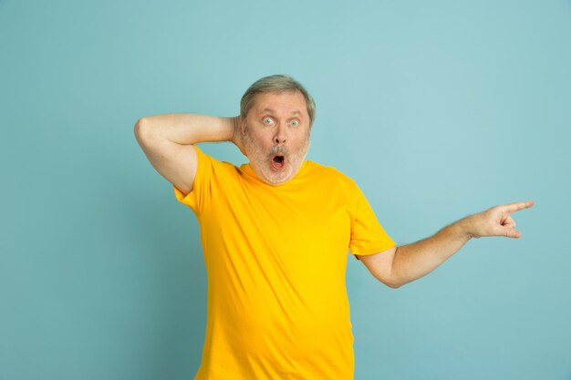 Shpcked wijzend naar de zijkant. Blanke man portret geïsoleerd op blauwe studio achtergrond. Mooi mannelijk model in geel overhemd poseren.