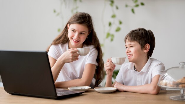 Siblings die thee drinken en laptop met behulp van