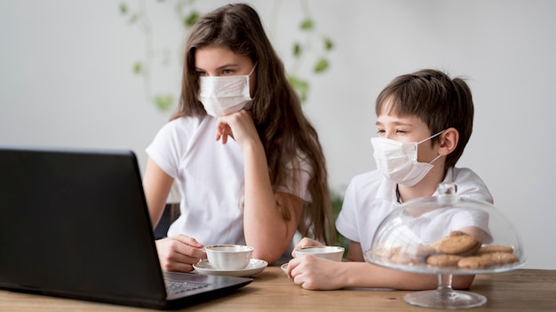 Siblings met masker dat op laptop kijkt