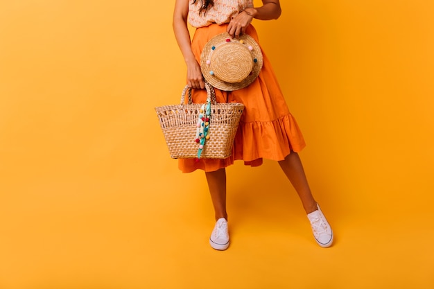 Sierlijk gelooid meisje met zomer tas poseren in studio. Zorgeloos vrouwelijk model in lange rok met trendy hoed.