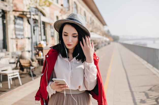 Sierlijke blanke vrouw kijken naar telefoon terwijl tijd buiten doorbrengen