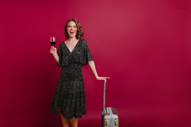Sierlijke kortharige vrouw met glas champagne poseren op een donkere achtergrond en lachen
