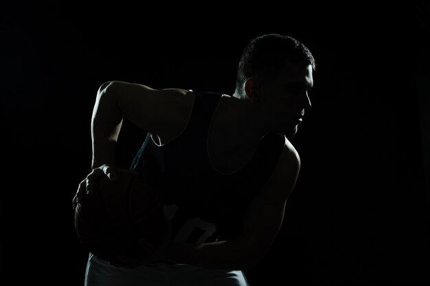 Silhouet van basketbal speler die de bal op zwarte achtergrond