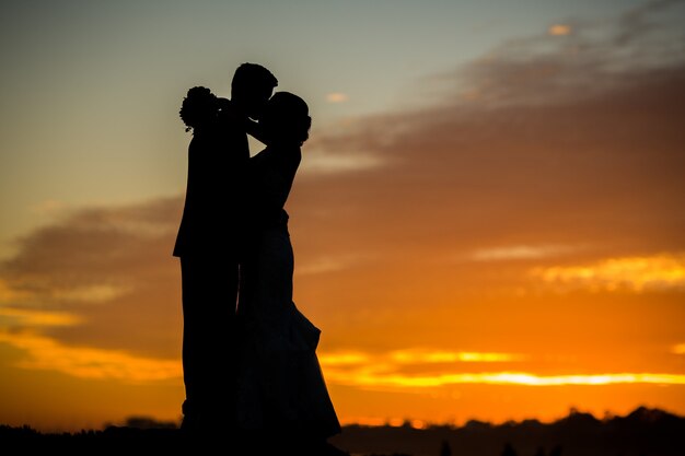 Silhouet van bruid en bruidegom kussen tijdens zonsondergang