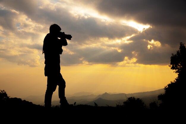 silhouet van een fotograaf die een zonsondergang in de bergen schiet