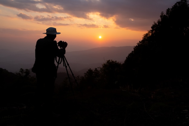 silhouet van een fotograaf die een zonsondergang in de bergen schiet