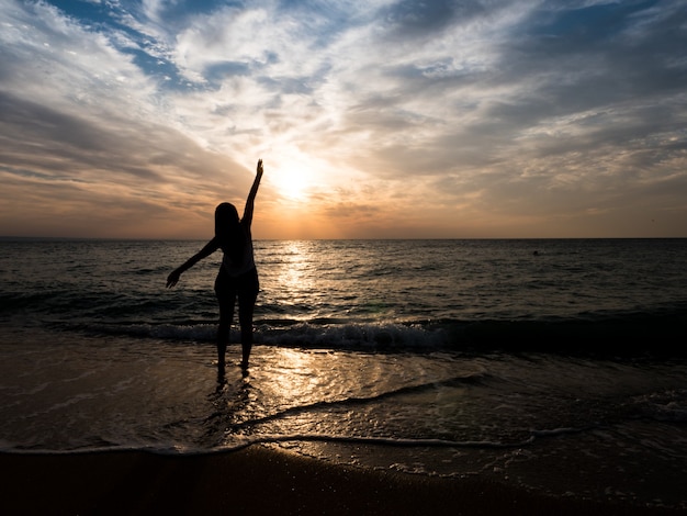 Silhouet van een jong meisje op het strand. jong meisje loopt bij zonsondergang aan zee. Toeristische meisje op strandvakantie.