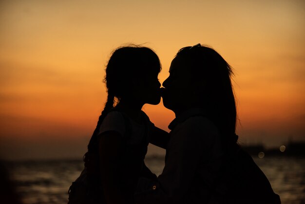 Silhouet van een jonge moeder die veel liefs haar dochtertje kust
