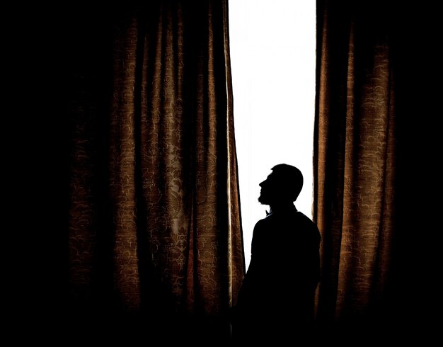 Silhouet van een man die voor een helder raam staat