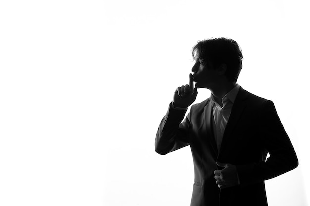 Silhouet van een man in een streng pak die vraagt om een stille schaduw te zijn, verlicht op een witte achtergrond