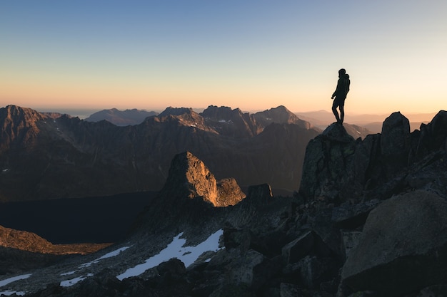 Gratis foto silhouet van een persoon die 's ochtends op de top van een heuvel onder de prachtige kleurrijke lucht staat