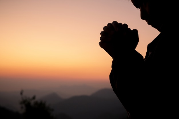 Silhouet van meisje die over mooie hemelachtergrond bidden.