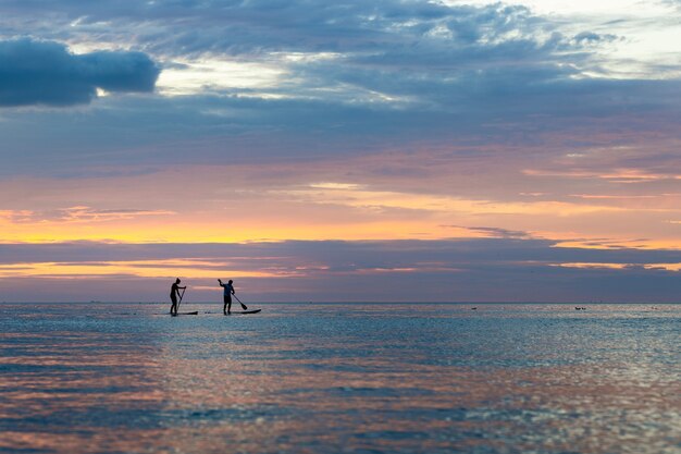 Silhouet van mensen paddleboarding tijdens zonsondergang