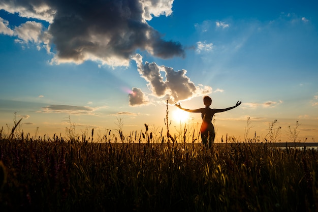 Gratis foto silhouet van sportieve meisje beoefenen van yoga in veld bij zonsopgang.