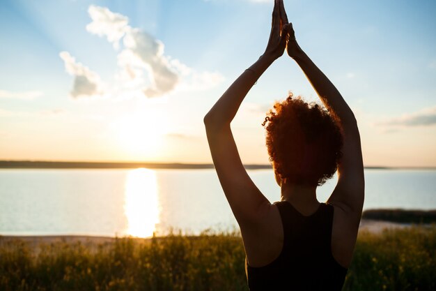 Silhouet van sportieve meisje beoefenen van yoga in veld bij zonsopgang.