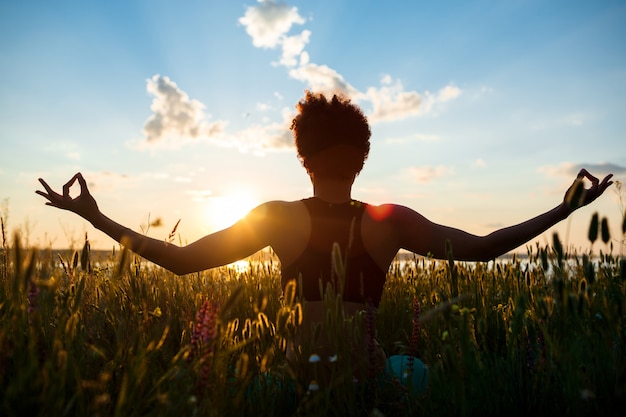 Gratis foto silhouet van sportieve meisje beoefenen van yoga in veld bij zonsopgang.