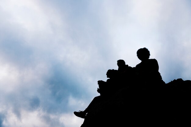 Silhouet van vrienden die op rots tegen blauwe hemel zitten