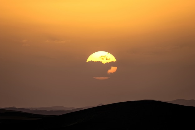 Silhouet van zandduinen met de zon achter een wolk