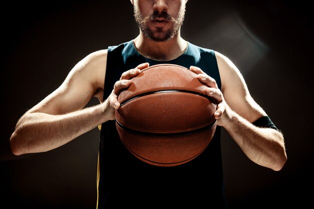 Silhouetmening van een basketbalbal van de de holdingsmand van de basketbalspeler op zwarte muur