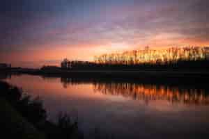 Gratis foto silhouetten van bomen onder de bewolkte avondrood weerspiegeld in het meer hieronder