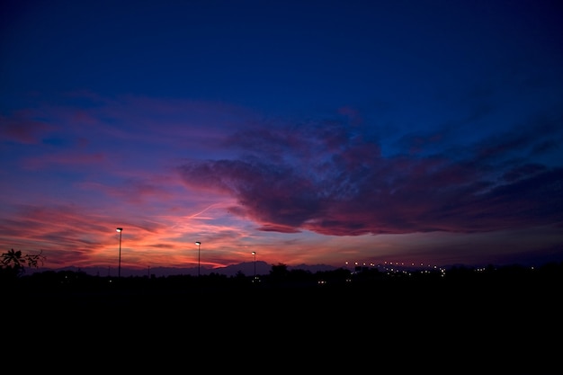 Gratis foto silhouetten van heuvels en straatlantaarns onder een bewolkte hemel tijdens een prachtige zonsondergang