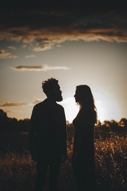 Silhouetten van jong koppel staande in een veld tijdens zonsondergang