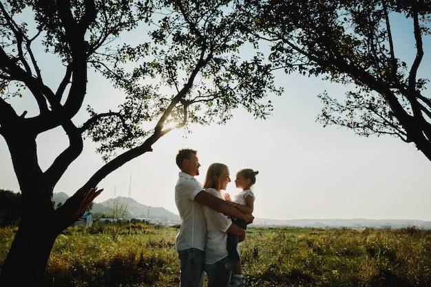 Silhouetten van mooie ouders die met hun dochter onder oude bomen spelen