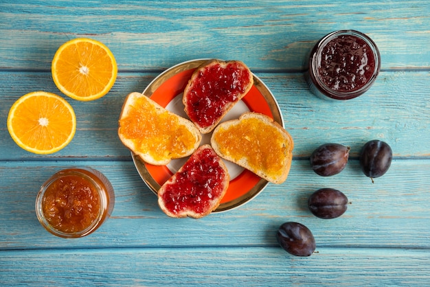 Gratis foto sinaasappel- en pruimconfituur in een glazen pot en op de toastbroodjes in een bord.