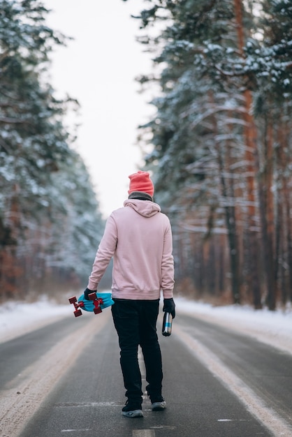 Skateboarder die op de weg staat midden in het bos omringd door sneeuw