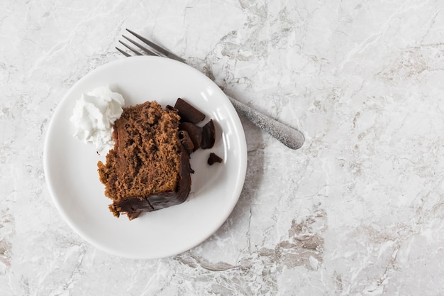 Slagroom en plak van cake op plaat met vork over de marmeren teller