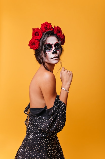 Slank donkerharige meisje met mooie houding poseren in jurk, ontblote schouders. Portret van mysterieuze Mexicaanse dame met zombiemaskerademasker