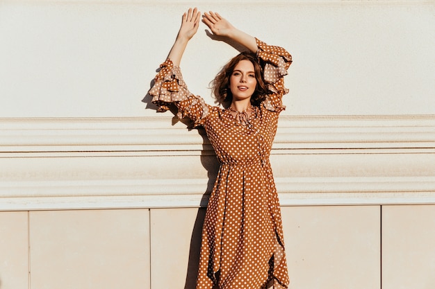 Slanke blanke vrouw met tatoeage poseren in elegante vintage jurk. Foto van geïnteresseerde dame met golvend haar draagt bruine jurk.