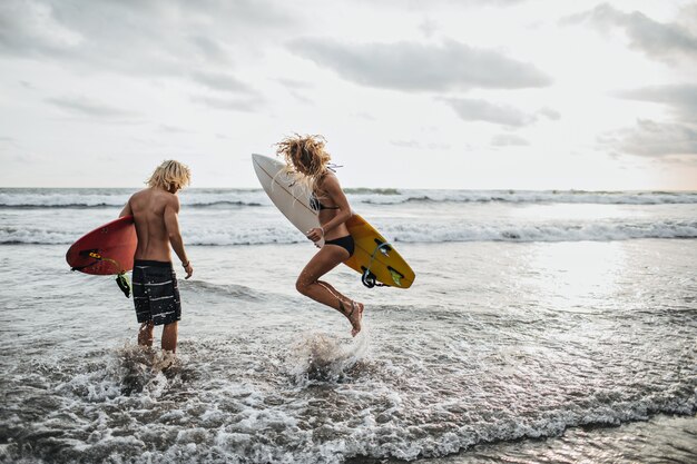 Slanke jongen en meisje springen in zeewater en houden surfplanken