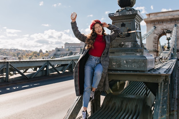 Slanke lachende vrouw in vintage jeans poseren op het platform achtergrond in zonnige dag in Parijs