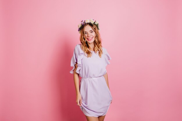 Slanke vrouw in mooie paarse jurk lachen op lichte muur