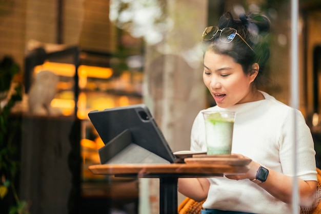 Slimme aantrekkelijke positieve Aziatische digitale nomade vrouw met casual doek werk op afstand nieuwe normale levensstijl handgebruik tablet teleconferentie onlive videogesprek vergadering op afstand in coffeeshop café