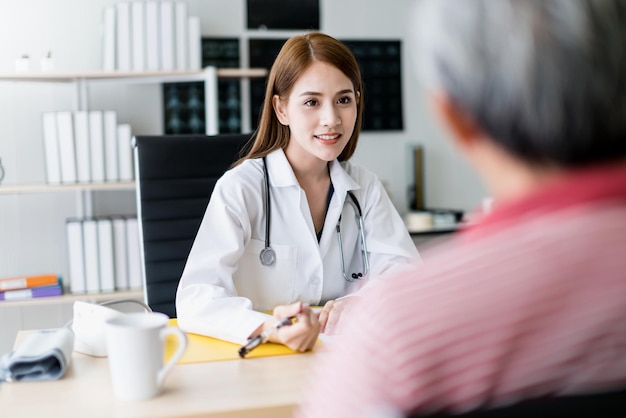 Slimme en aantrekkelijke aziatische vrouwelijke arts legt uit en bespreekt met de oude aziatische man om het achtergrondgezondheidsconcept van de kliniek te raadplegen