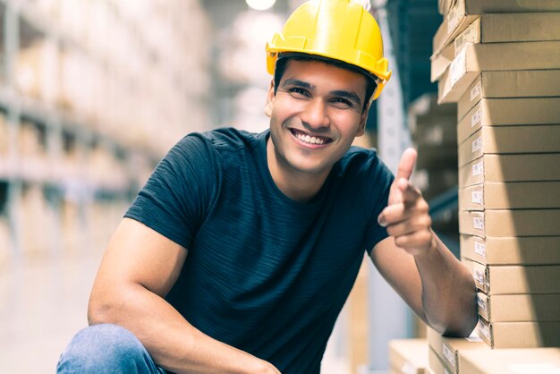 Slimme Indiase ingenieur met een veiligheidshelm die de voorraadcontrole en het productbeheer van de kartonvoorraad doet op de achtergrond van het fabrieksmagazijn