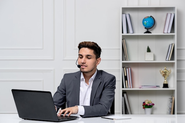 Slimme knappe kerel van de klantenservice met laptop in grijze kantoorblazer die een verzoek typt