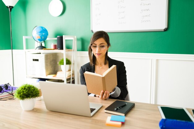 Slimme leraar die een boek voorleest aan haar online studenten. Jonge vrouw die een dictaat geeft in een virtuele klas