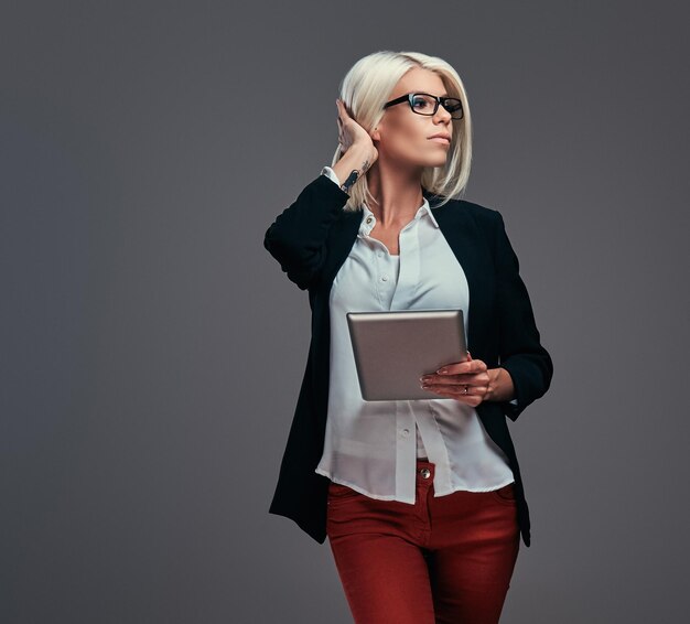 Slimme modieuze blogger vrouw in moderne kleding en bril, poseert met digitale tablet. Geïsoleerd op een grijze achtergrond.