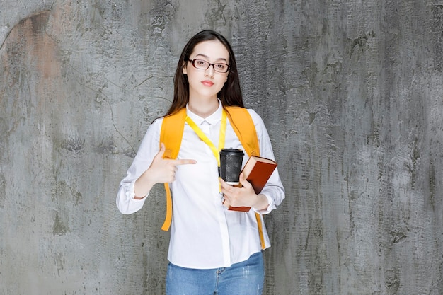 Slimme vrouwelijke student in glazen met boek en kopje koffie staan. hoge kwaliteit foto